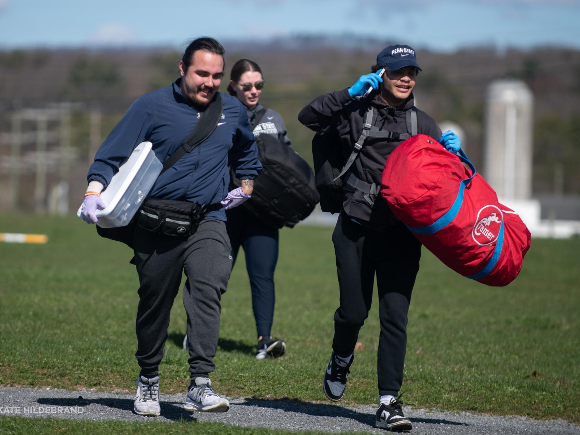 Three athletic training students walk across a field carrying medical equipment. 