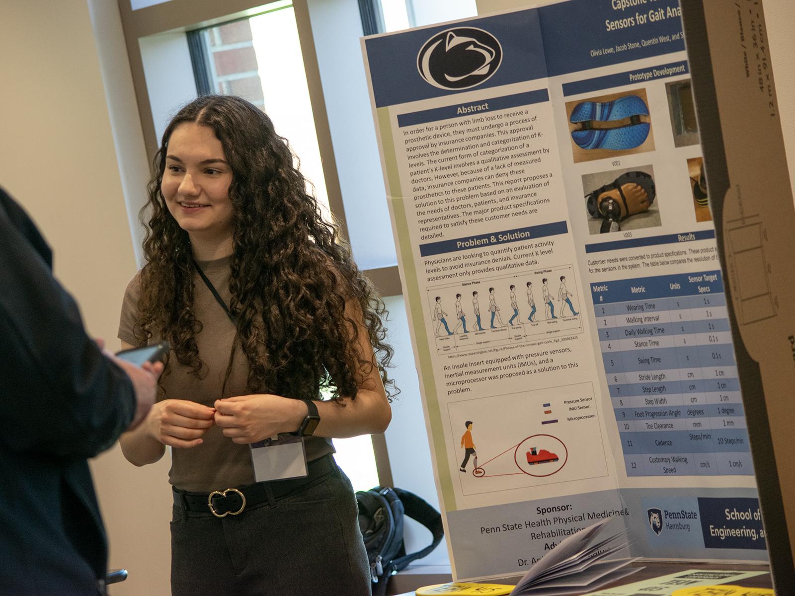 A student stands next to a research poster at the Capstone Design Conference