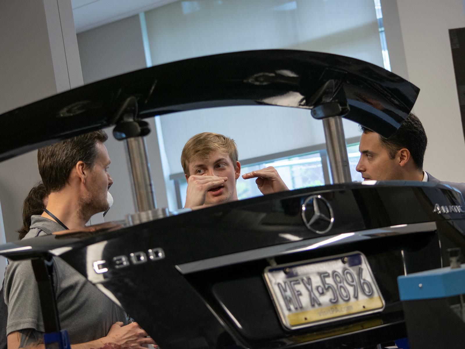 Students and faculty talk in the background of a car trunk lid on display