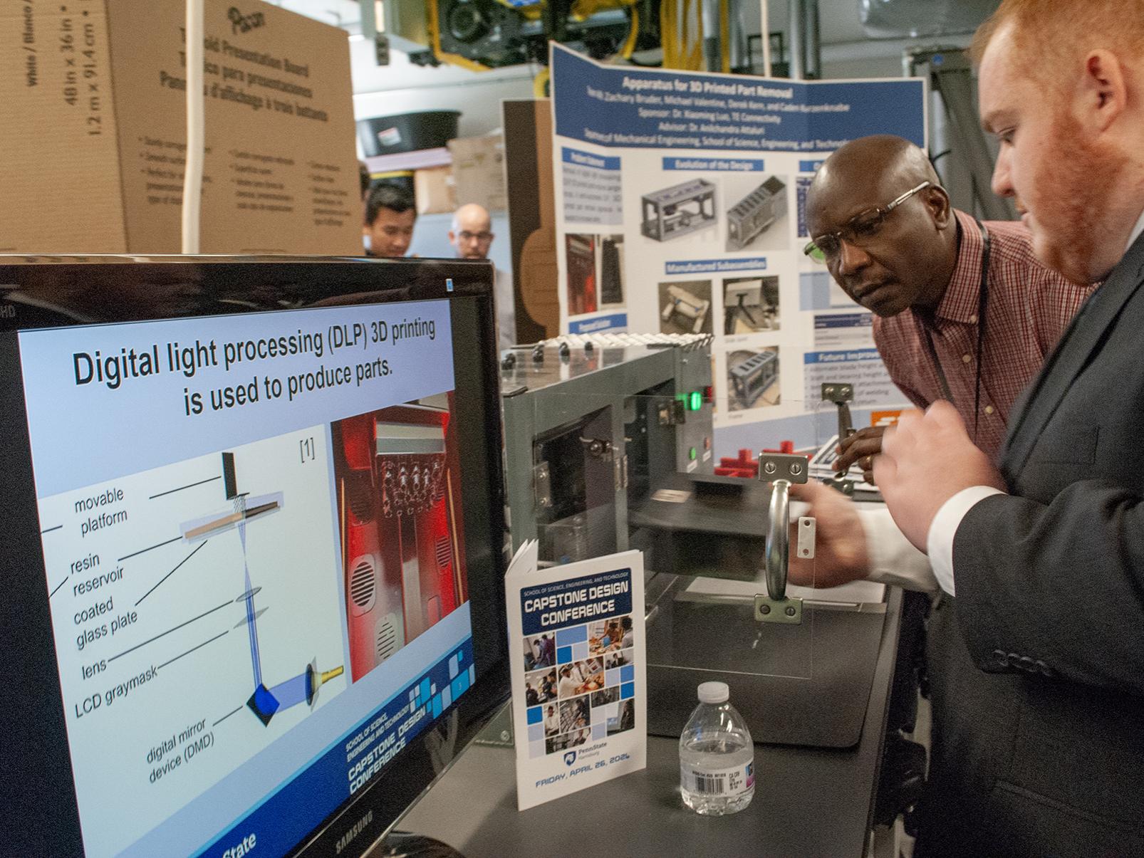 A student talks to a faculty member in front of a capstone project