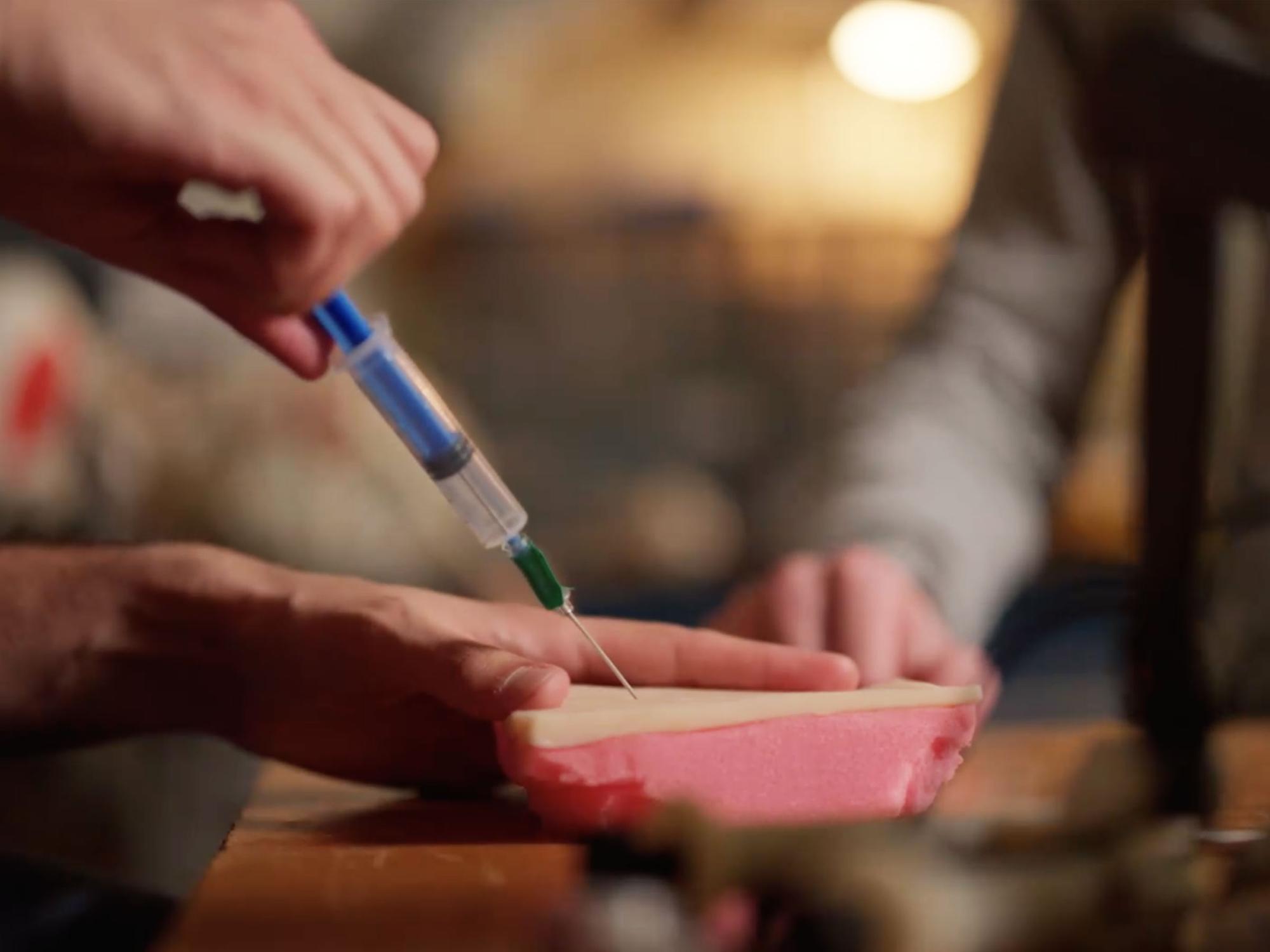 A student injecting a catheter into a simulated layer of skin attached to foam.