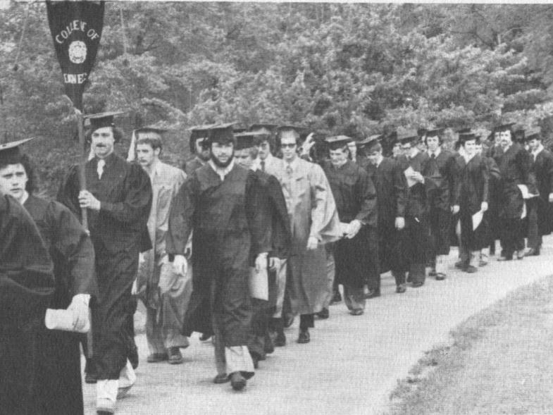 A group of graduates walks outside in their caps and gowns