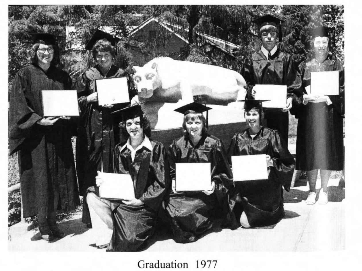 A group of graduates hold their diplomas in front of a lion statue