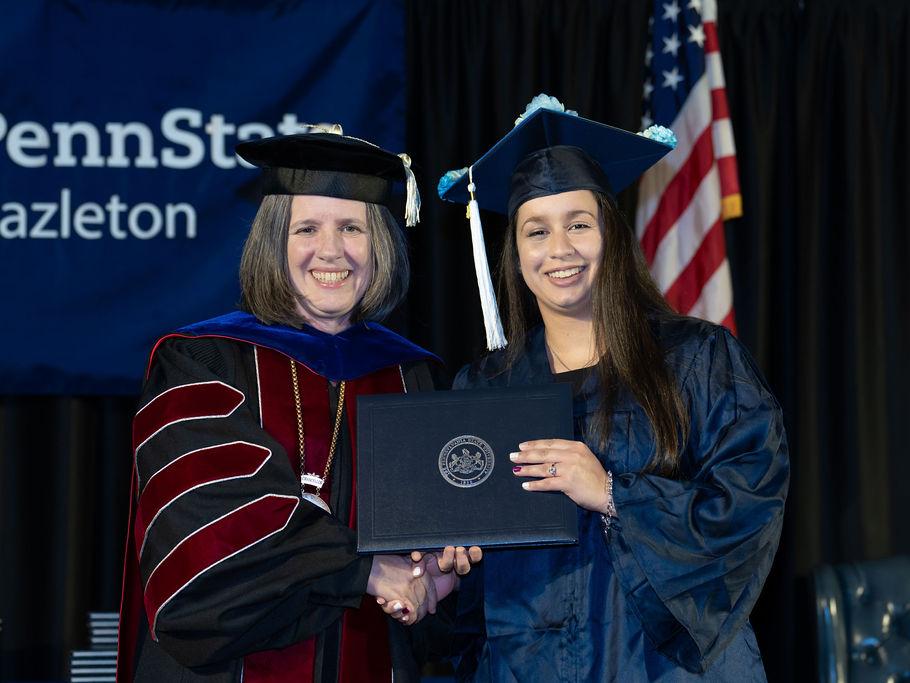 Graduate holding her diploma cover and shaking the hand of the chancellor.