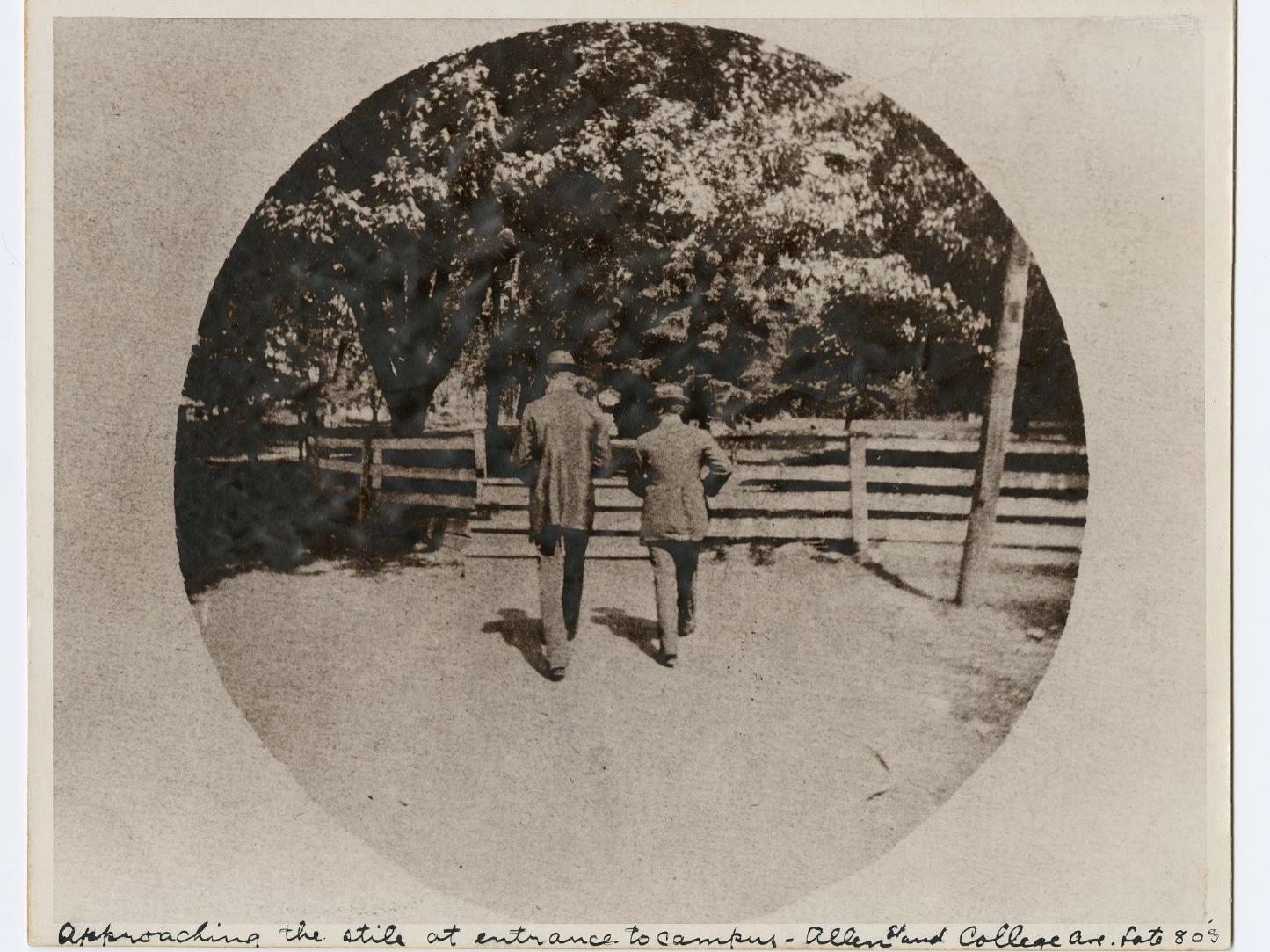 The backs of two men in front of a wooden fence in the 1880s.