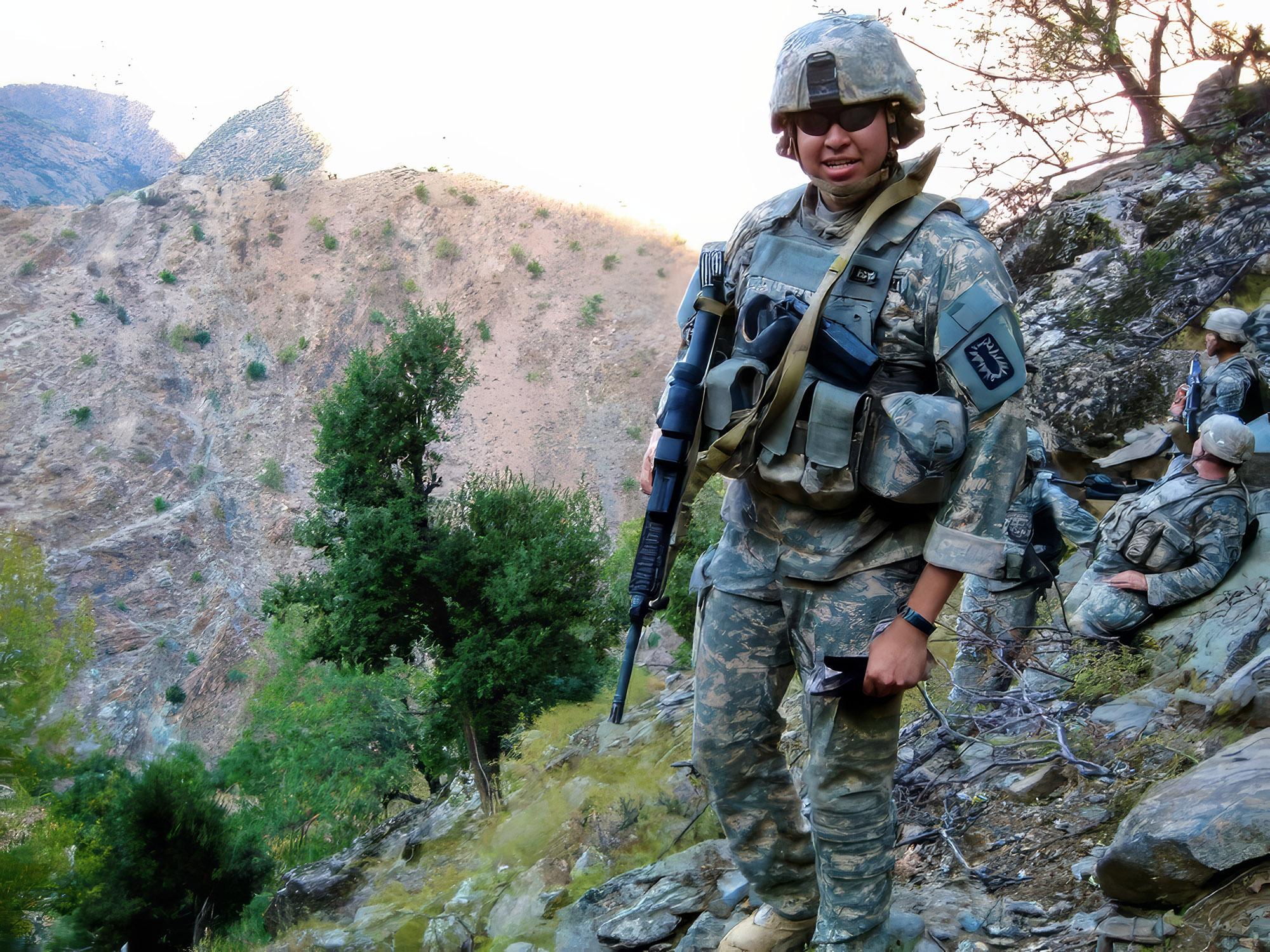 a man in camouflage stands on a hillside with a mountain in the background