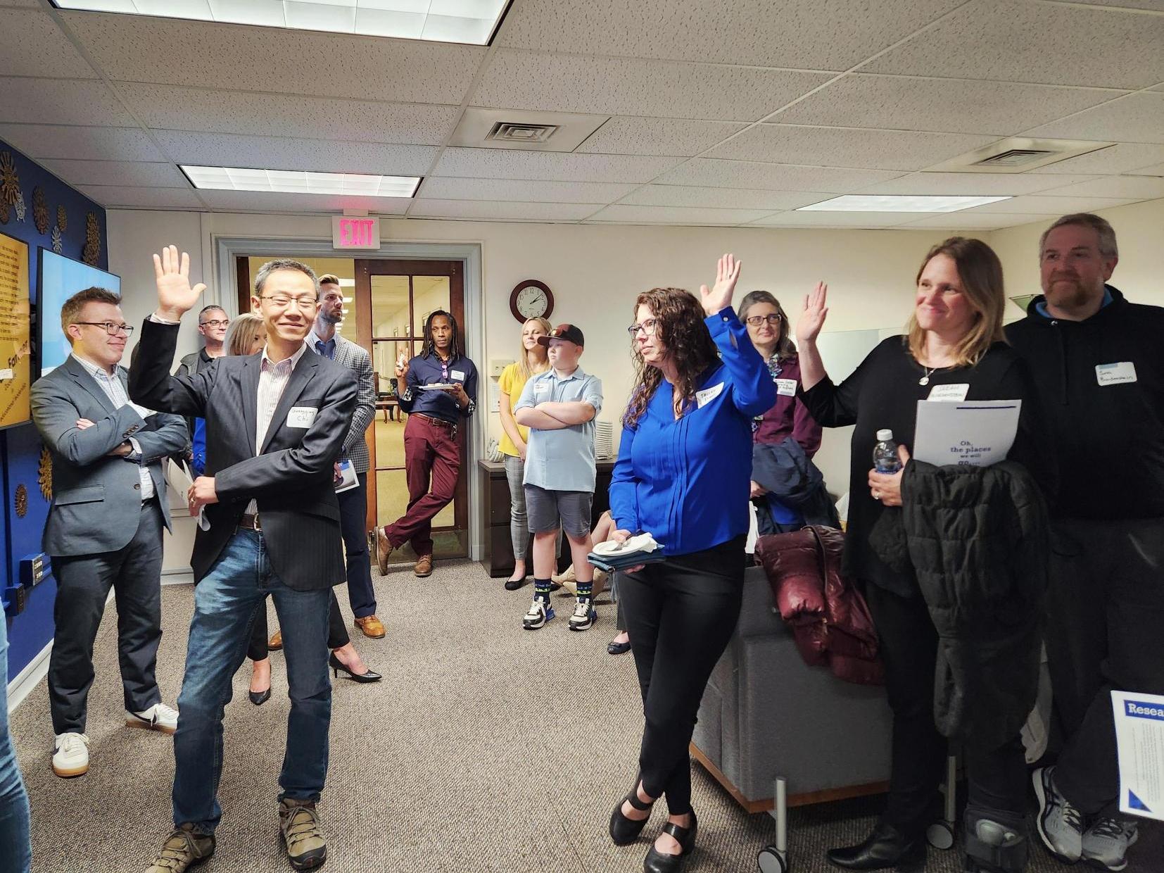 Group of people standing in an office, some have their hands raised. 