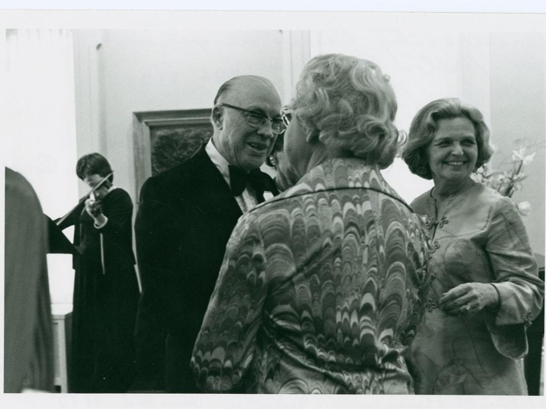 A black and white picture of a man wearing a tuxedo talking to a woman