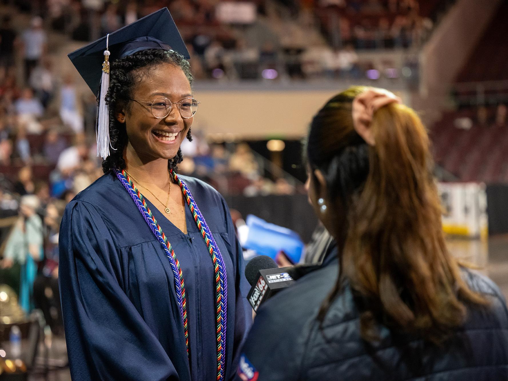 A Penn State Behrend graduate talks with a TV reporter before the college's commencement ceremony.