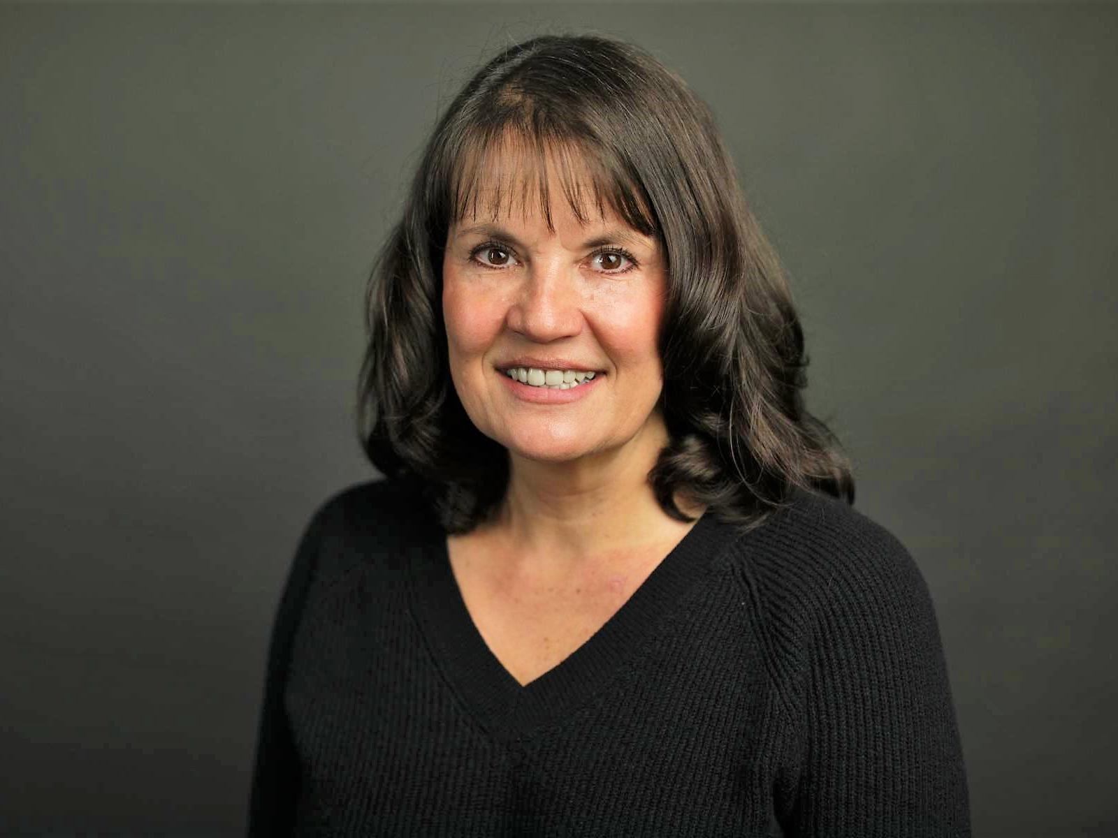 A woman with shoulder-length hair smiles in an official portrait photo.