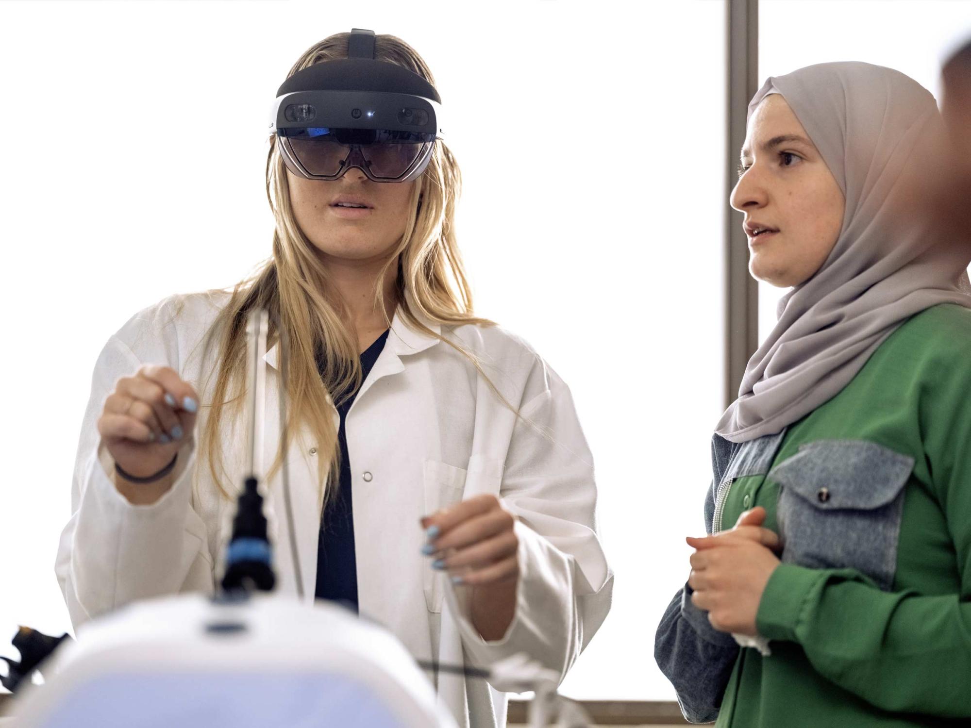 A student with a virtual reality headset on being coached by another student. 