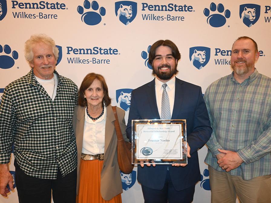 Four people standing against a backdrop with the Penn State Wilkes-Barre logo.