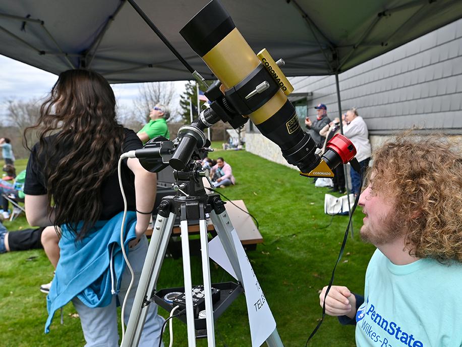 A man sitting under a telescope under a canopy.