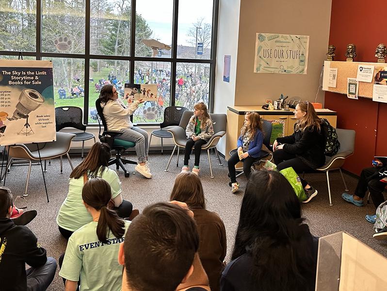 A woman holding up a book while reading a story to a room of people.
