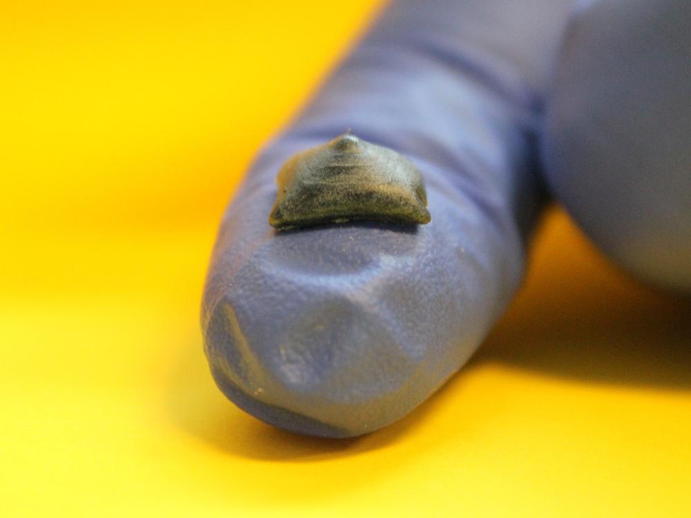 A small amount of material rest on the pad of a finger in a blue glove.
