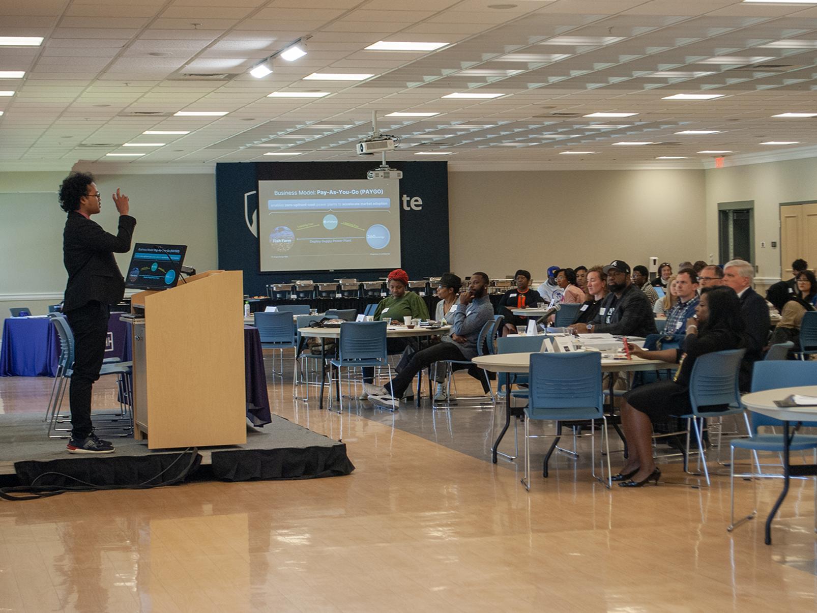 A student pitches a startup idea before a panel of judges and others