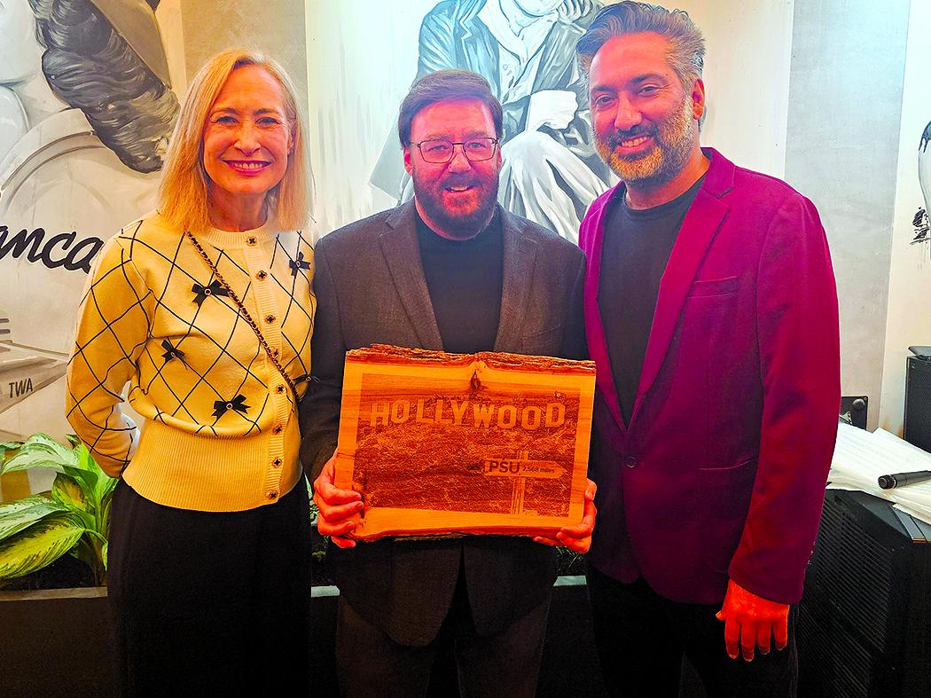 A woman wearing a white sweater and two men wearing dark sport coats stand together and smile