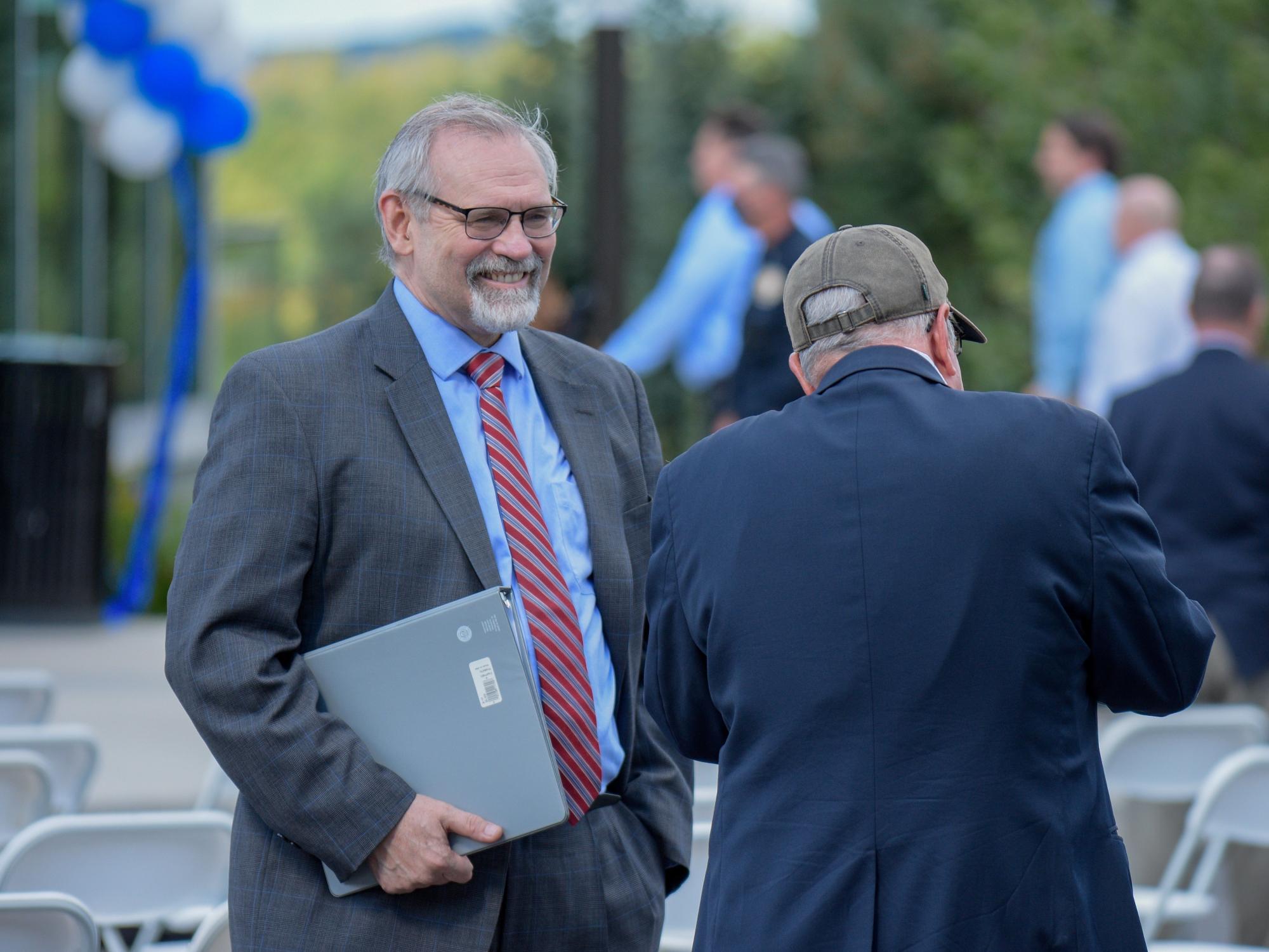 A man wearing a suit, holding a binder and smiling.
