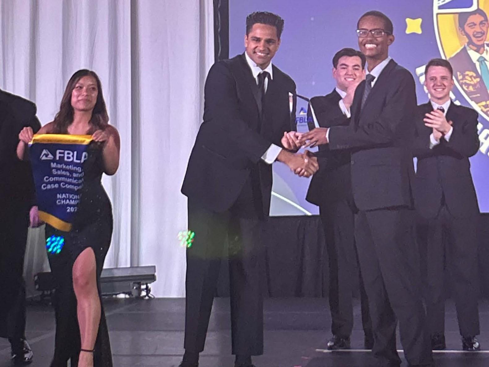A group of people in formal attire stand on a stage while an award is presented.
