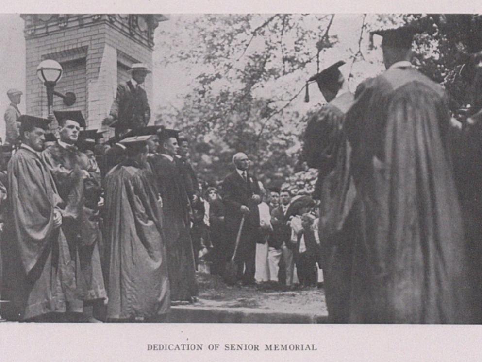 A group of students wearing caps and gowns near the main entrance to campus in 1916