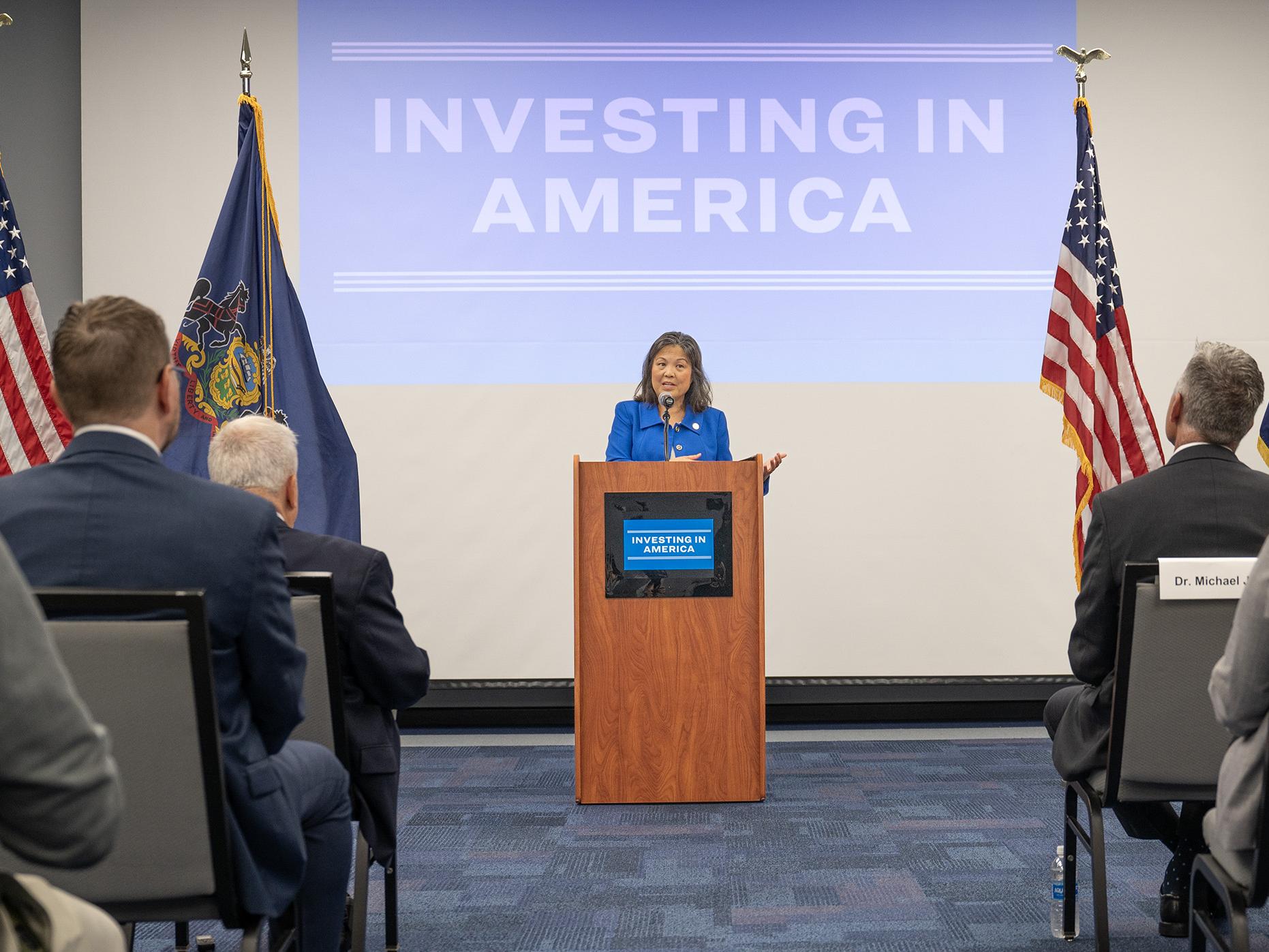 A person speaks at a podium to an audience in a conference room