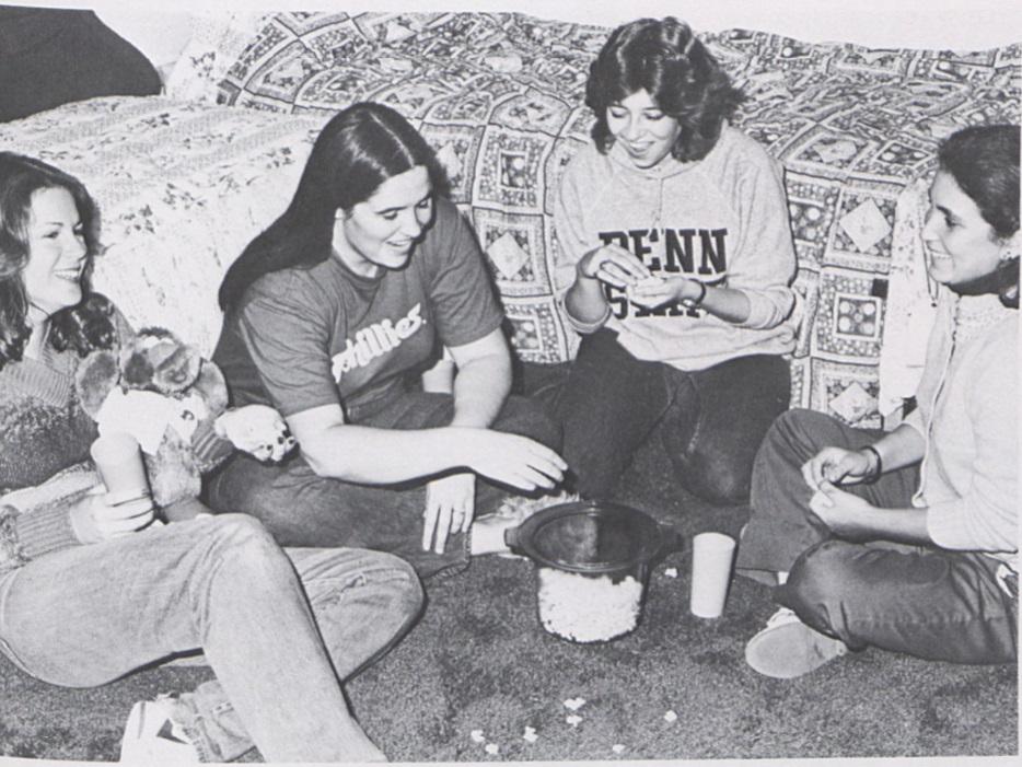 Four students sit on the floor of a dorm room and eat popcorn