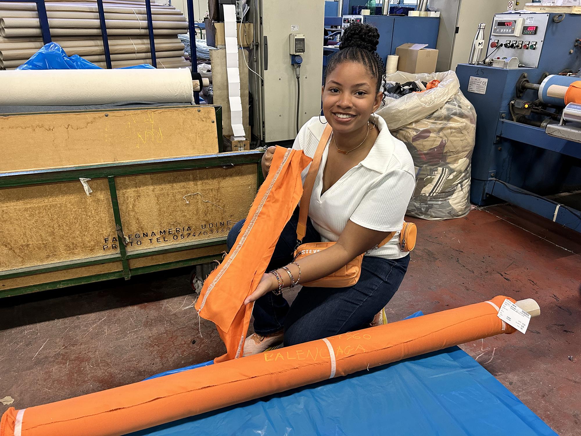 Elana Laing holding a piece of orange fabric in a textile factory