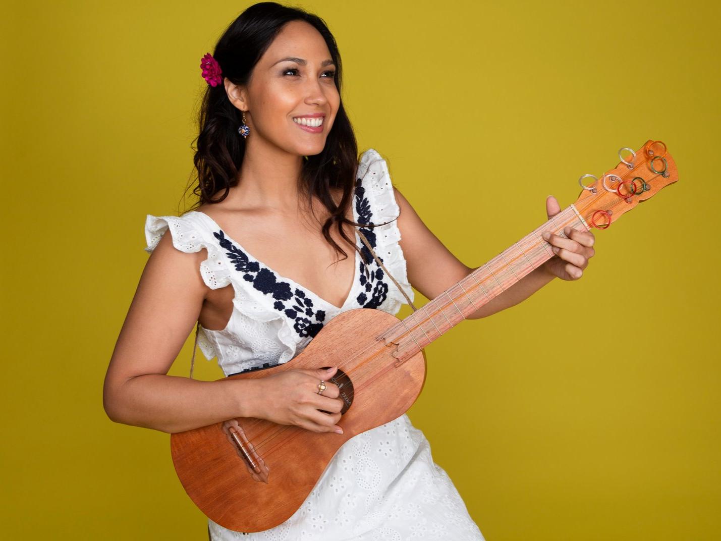 A woman smiles and plays a small guitar.