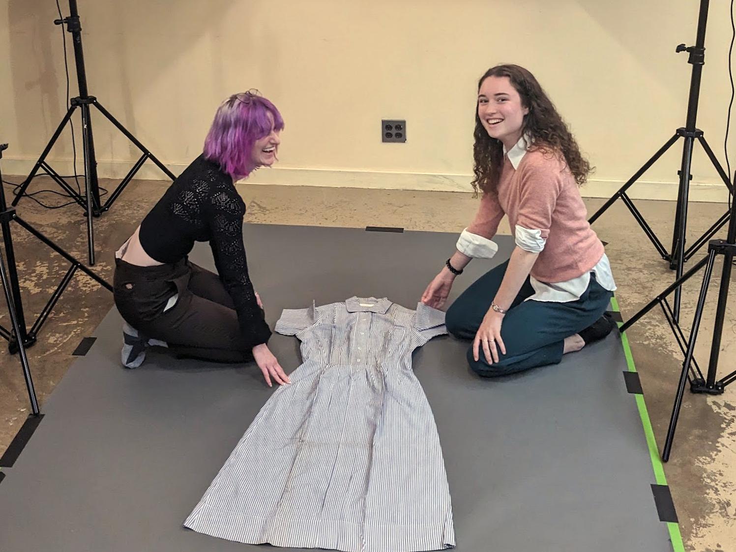 Two students sit on the floor, arranging a vintage dress to photograph