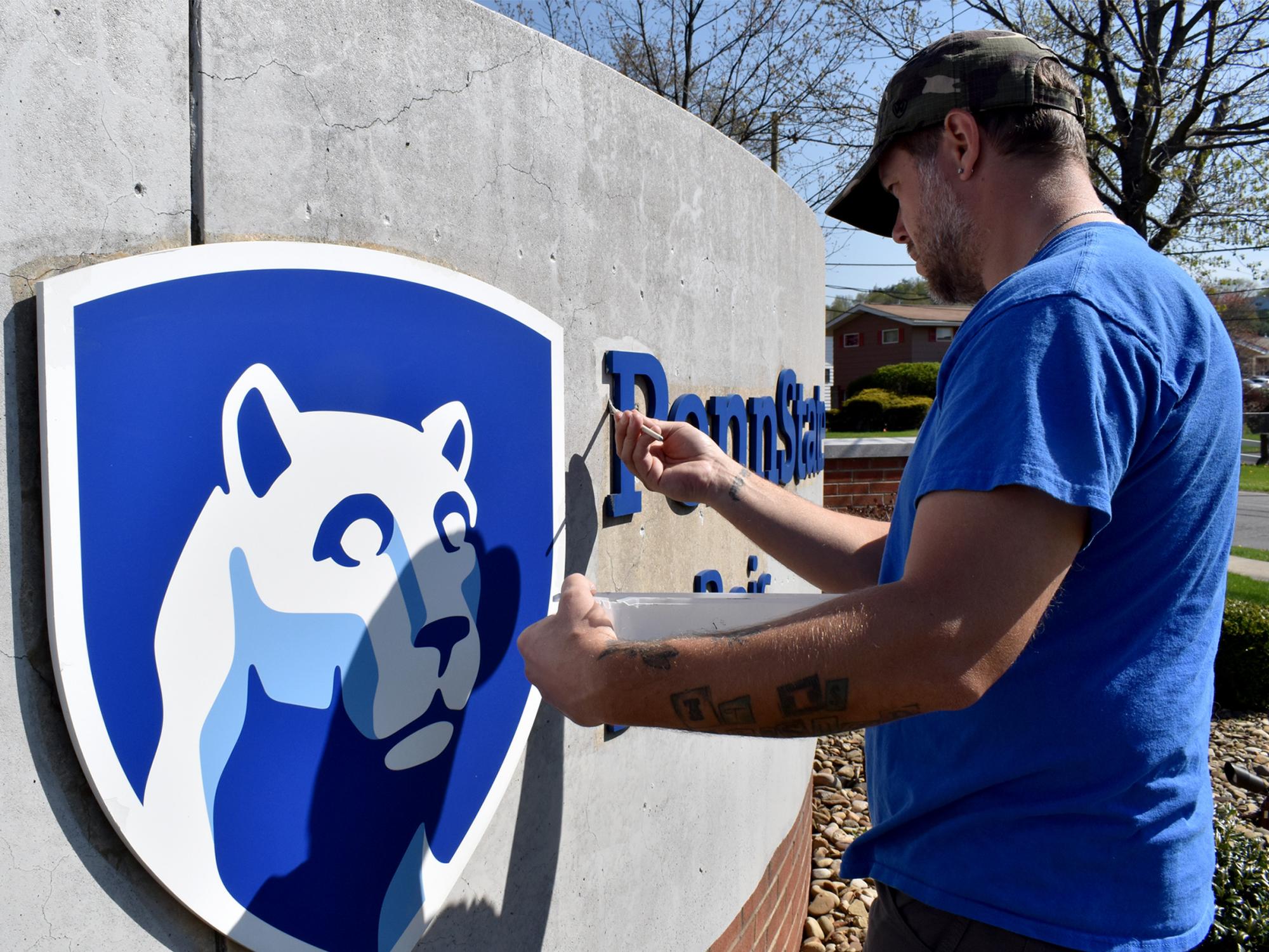 Building operations staff member Brooks Carr works through his first coat of paint during a refurbishment project on the entrance sign at Penn State DuBois.