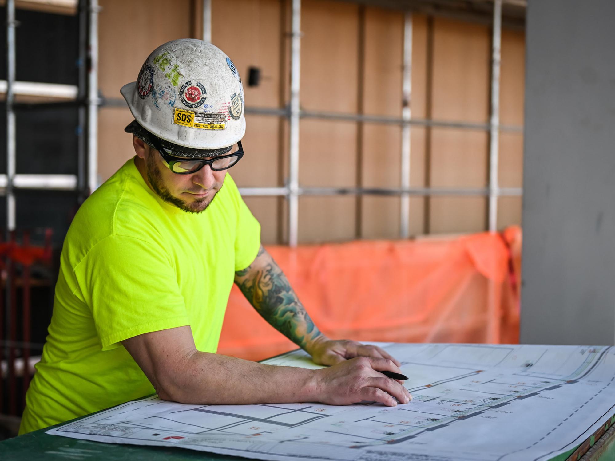person in construction hat looks over blueprints of new building