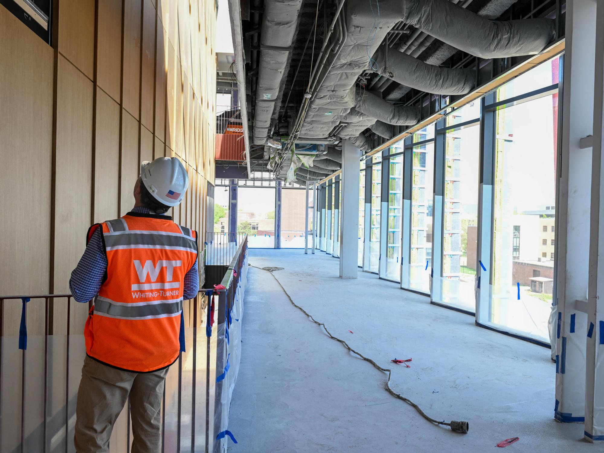 person in construction vest and hard hat inspects interior wall of building under construction