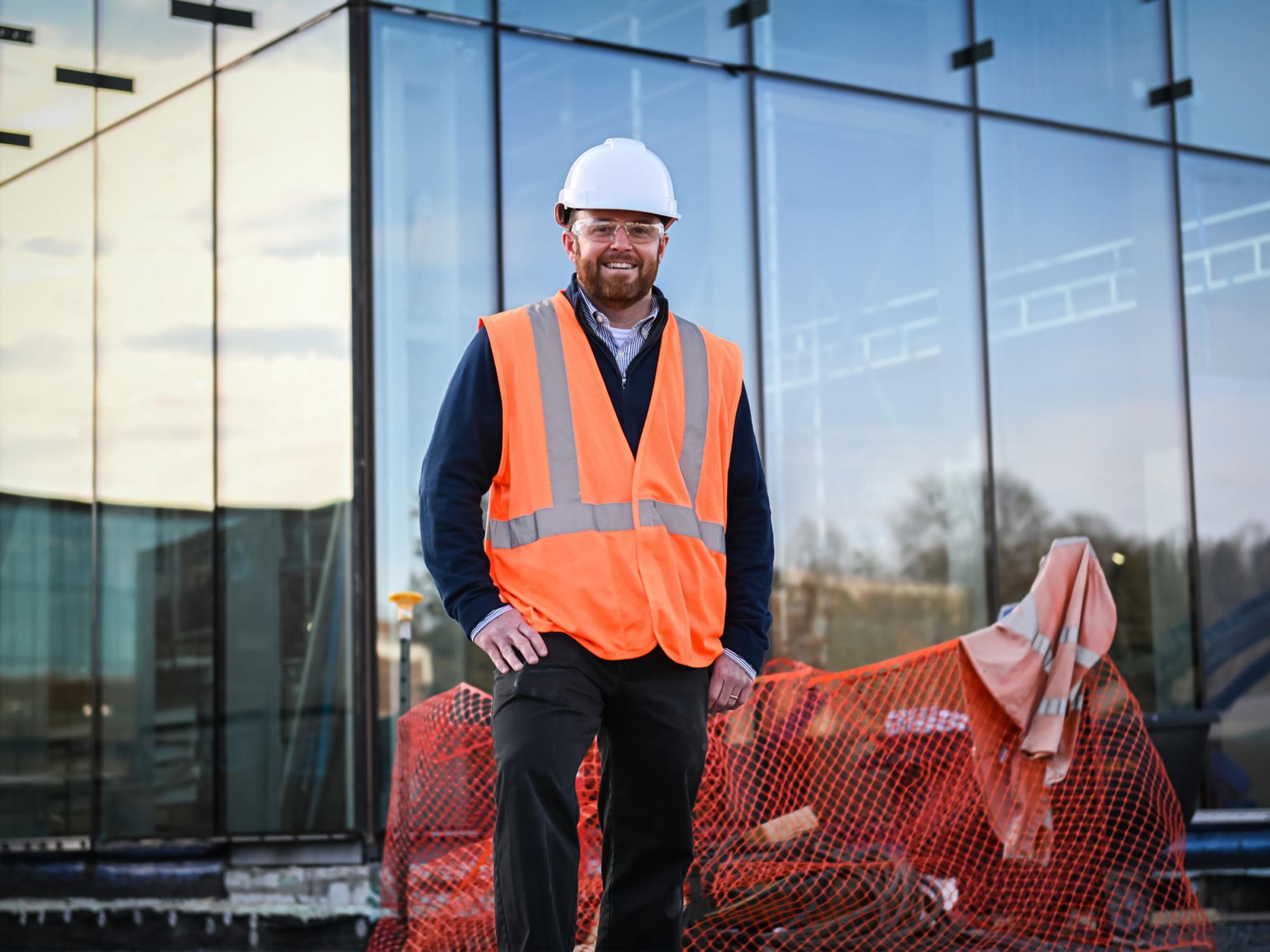 person in construction vest and hard hat poses for photo outside of building under construction