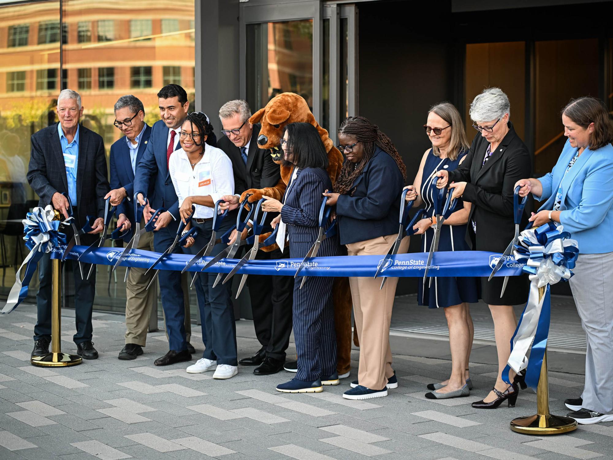 Ten people and one lion mascot cut ribbon with scissors to open new building