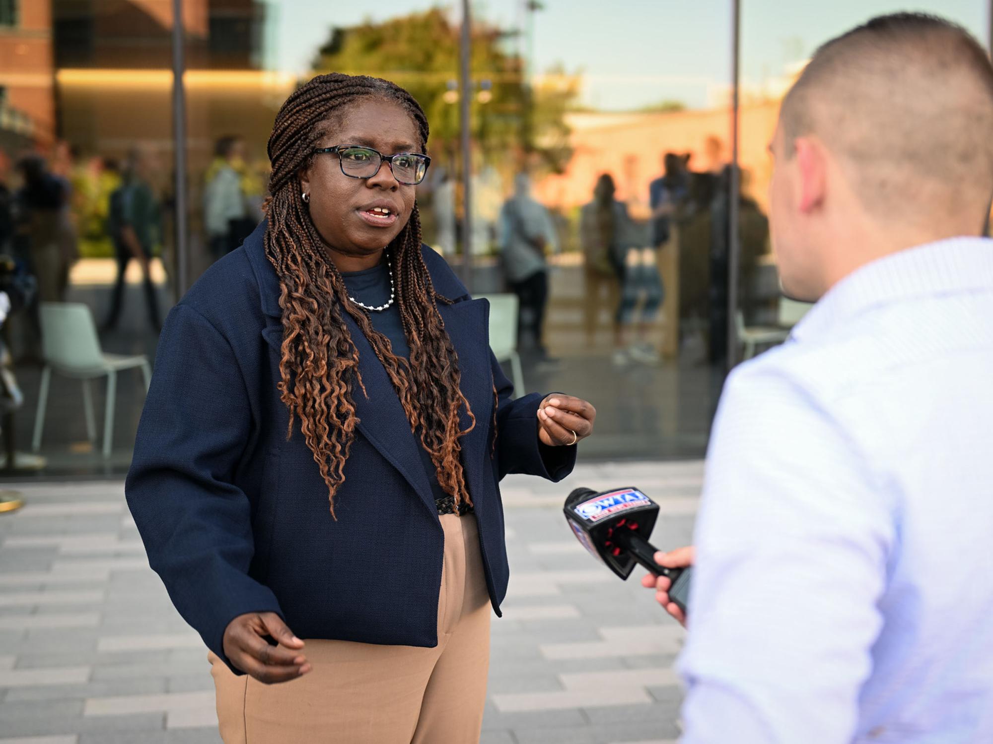 person speaking to journalist with microphone outside new building