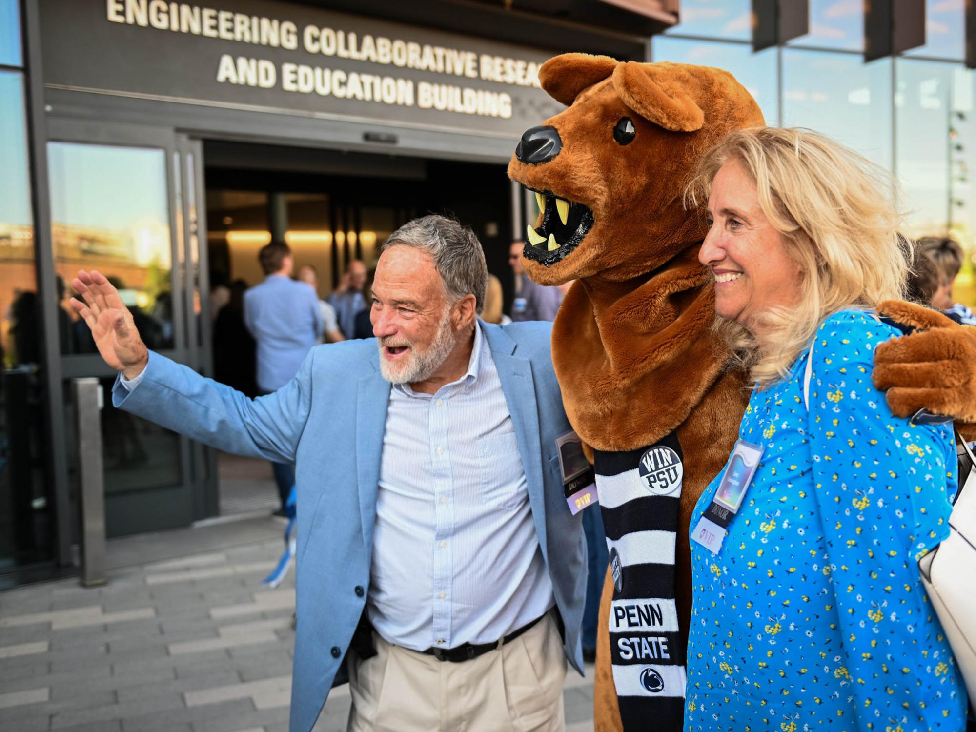 two people take a photo with lion mascot outside new building