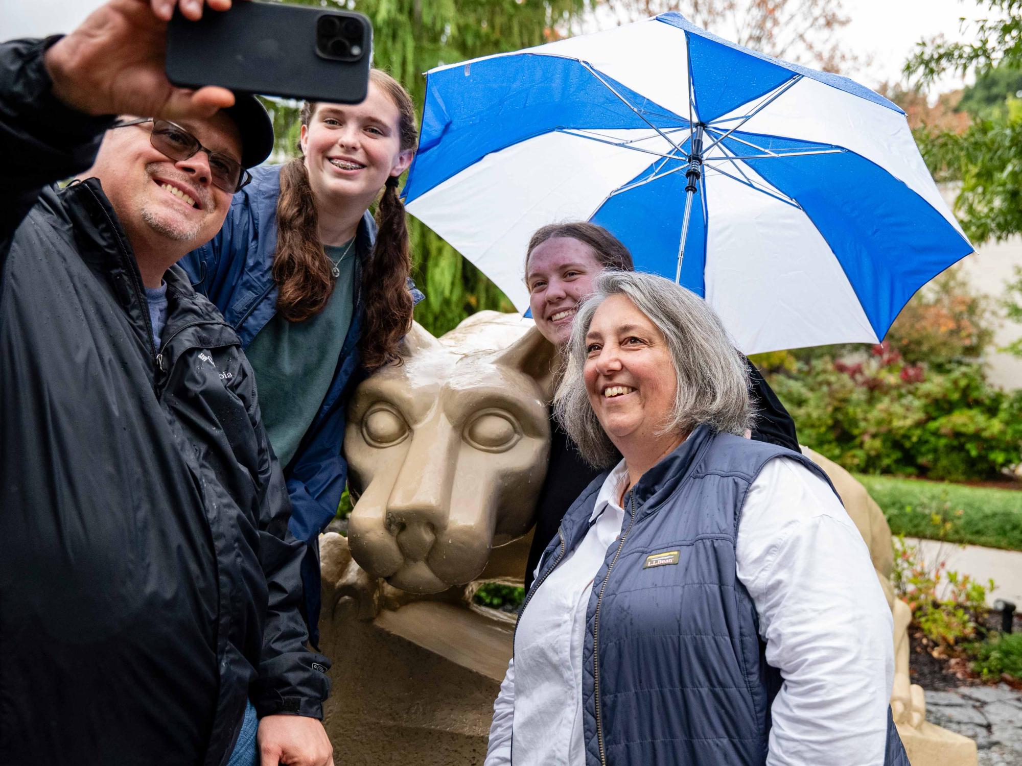 A family wearing rain gear and holding an umbrella poses for a selfie by the Berks lion shrine