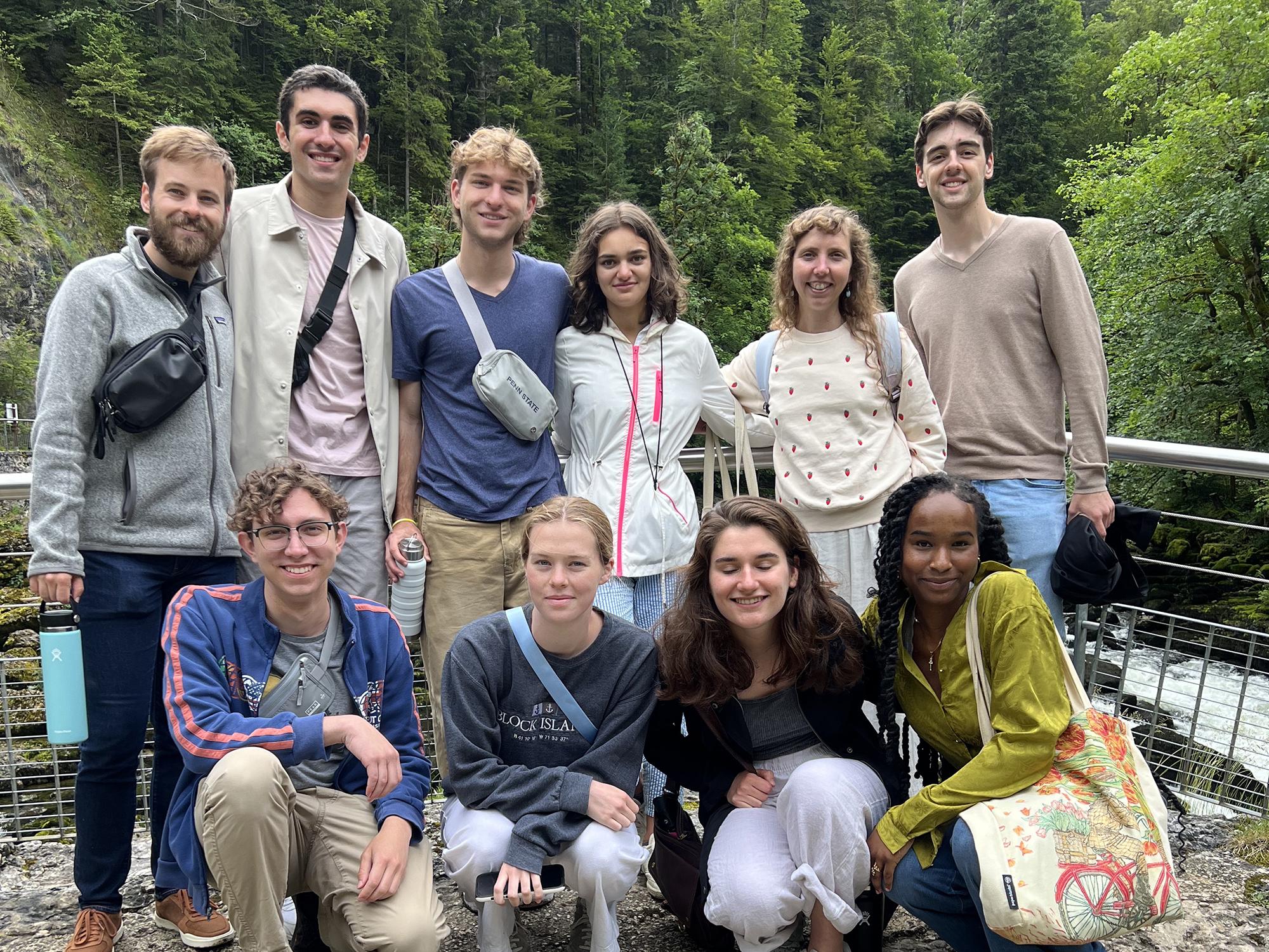A group of Penn State students poses in two rows in front of a waterfall with nice scenery behind them.
