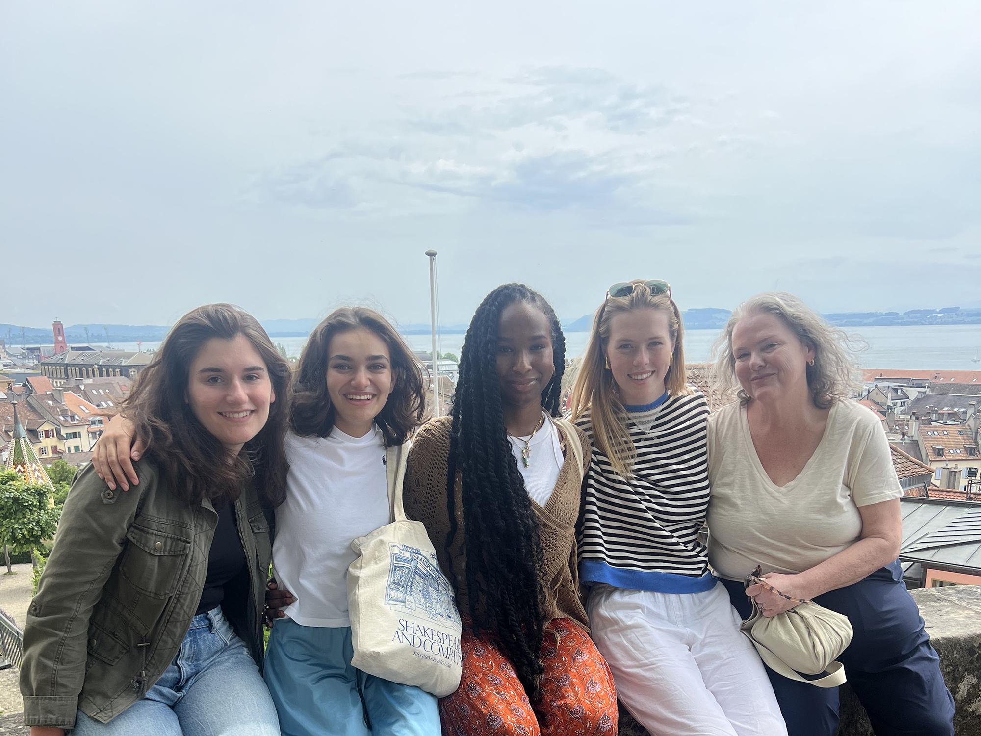 A group of four Penn State students and a faculty member sit on a ledge overlooking Neuchâtel, Switzerland. 
