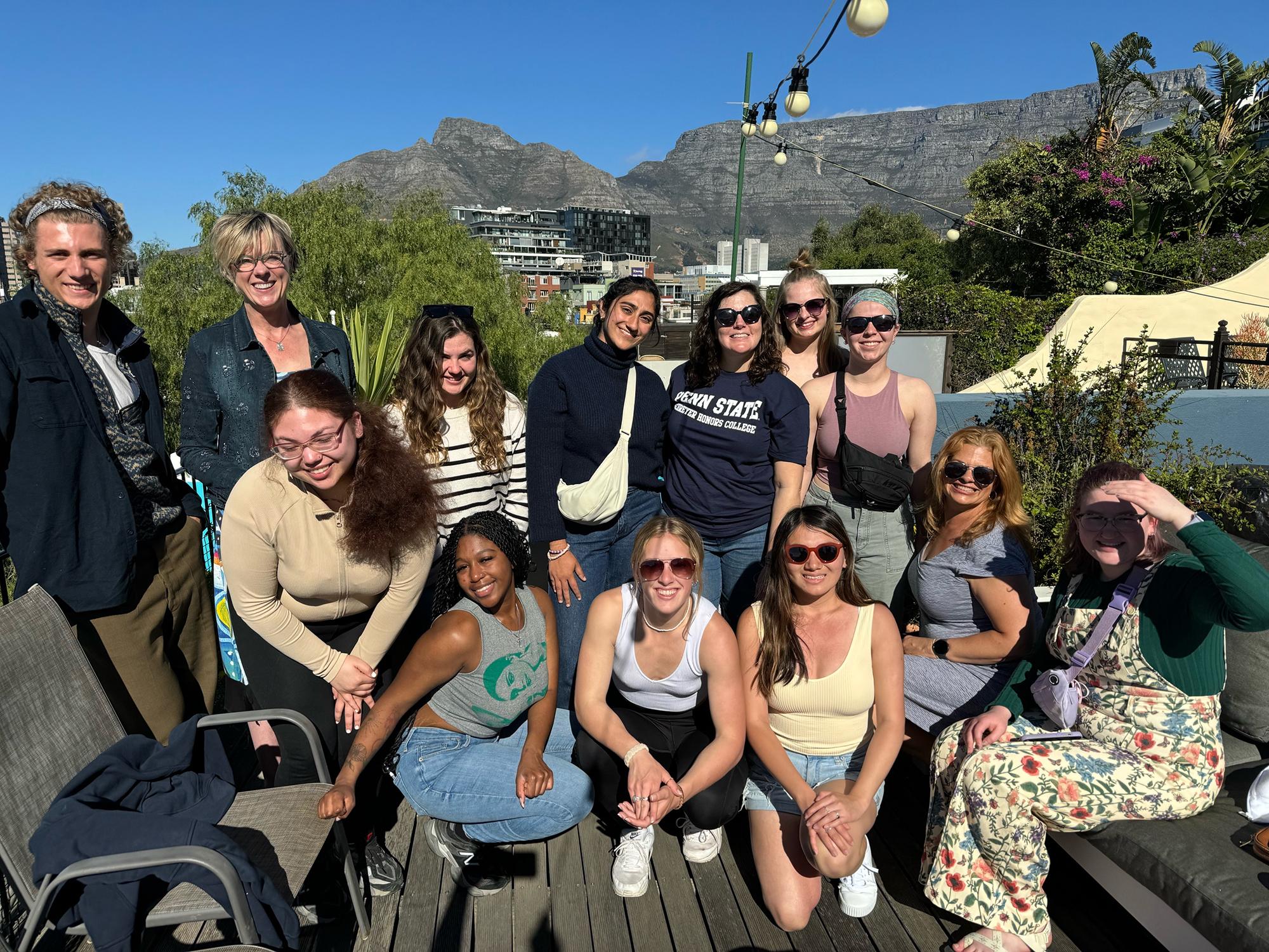 Students sit and stand in two rows on an outdoor patio in Cape Town, South Africa.