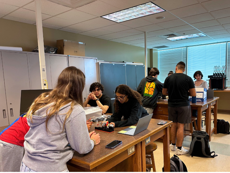 engineering students work on a project at long, wooden desks in a classroom