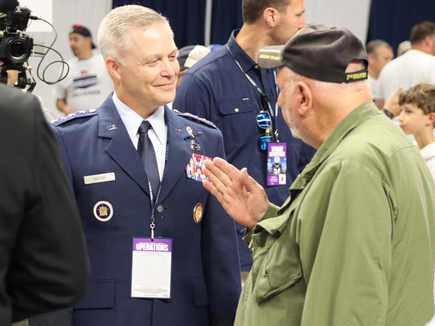 A man wearing a military uniform speaks with another man.