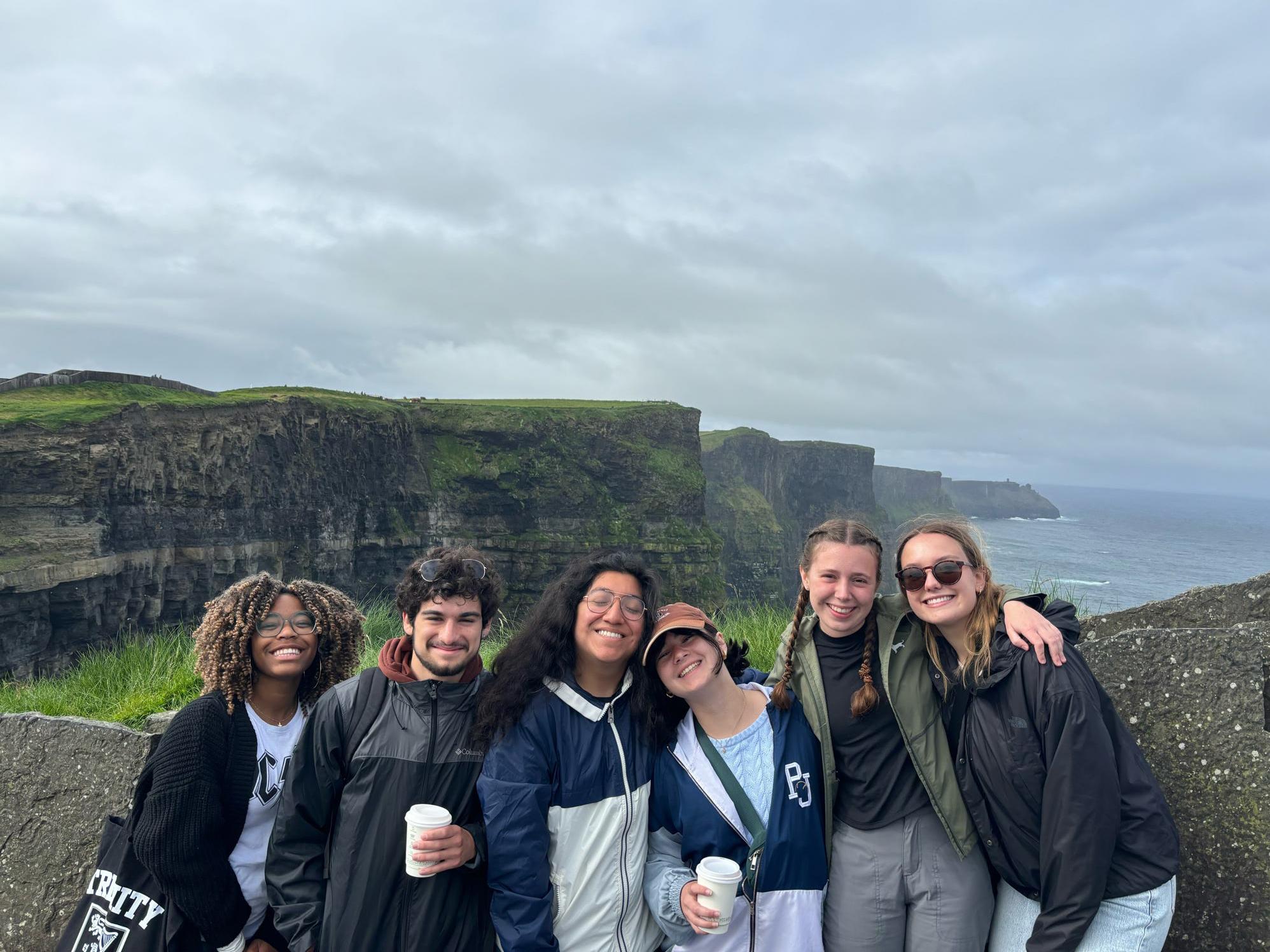 Students pose on the side of a mountain with rock formations and water behind them in Connemara National Park in Ireland.