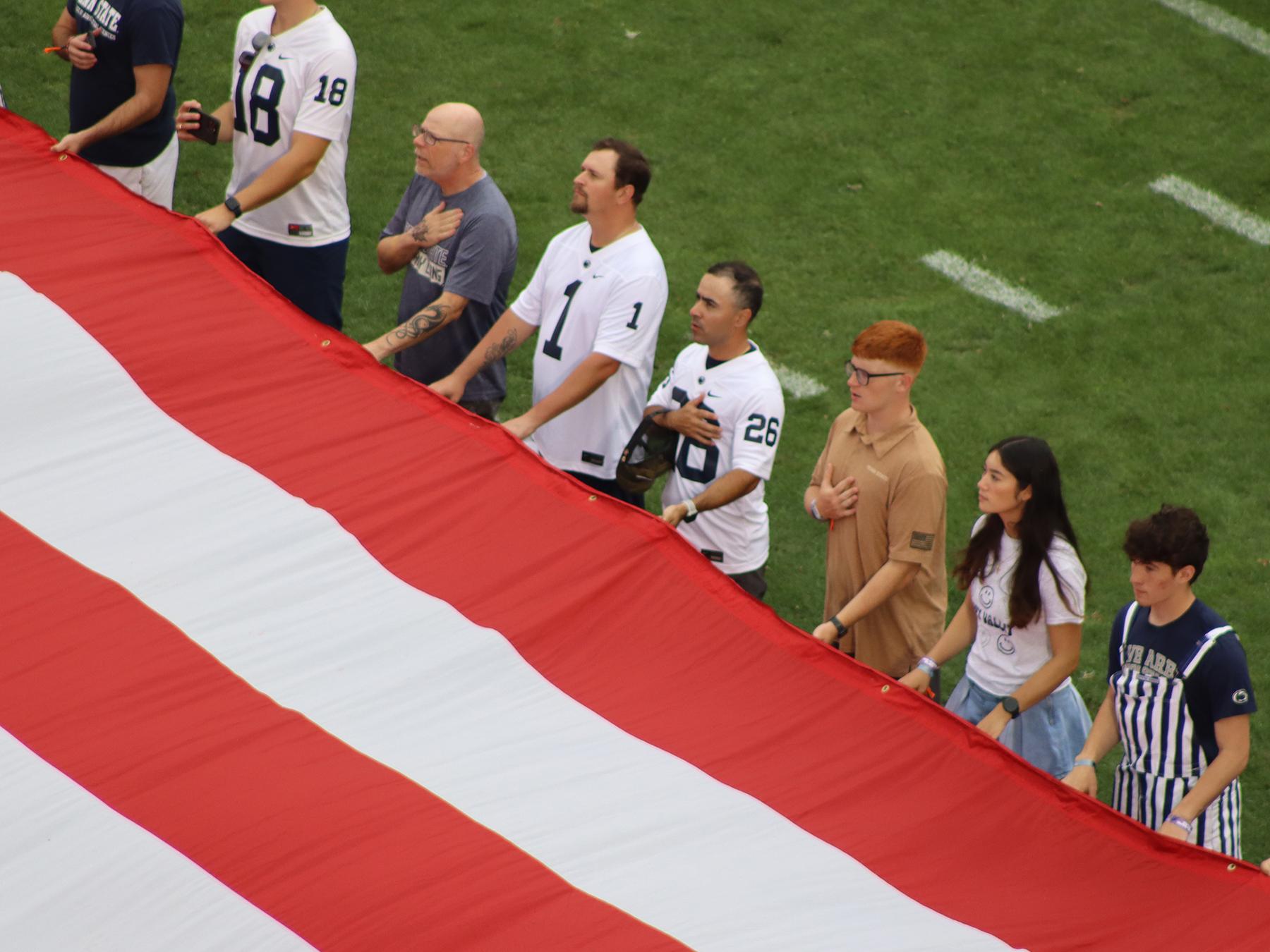A group of people holding a large American flag on a football field.