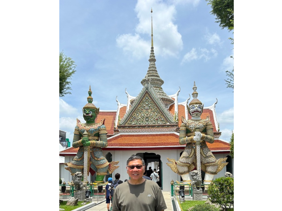 a man smiles in front of an ancient temple in Thailand