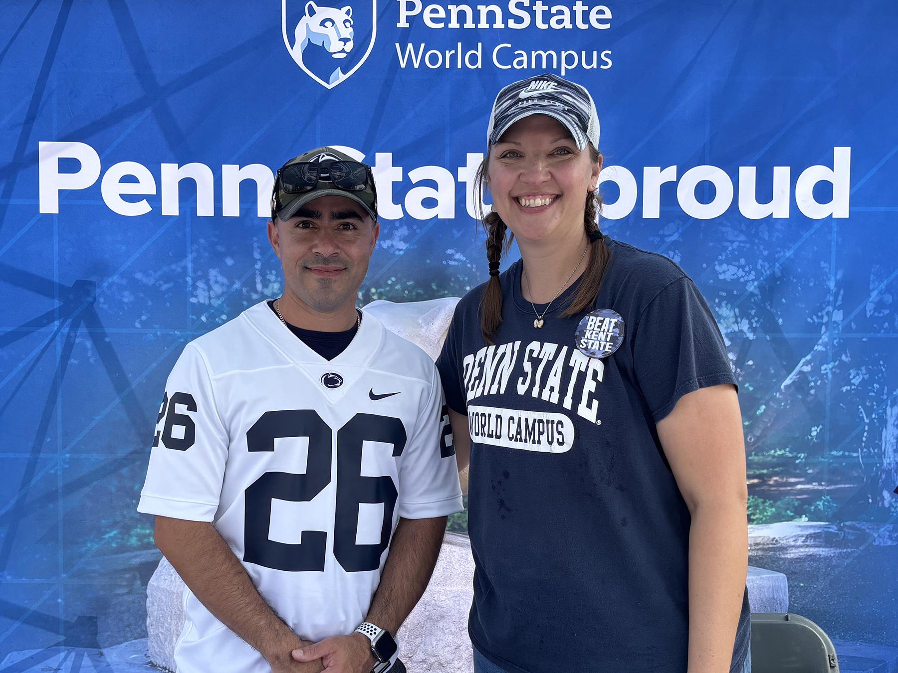 Two people pose in front of a Penn State-themed background.