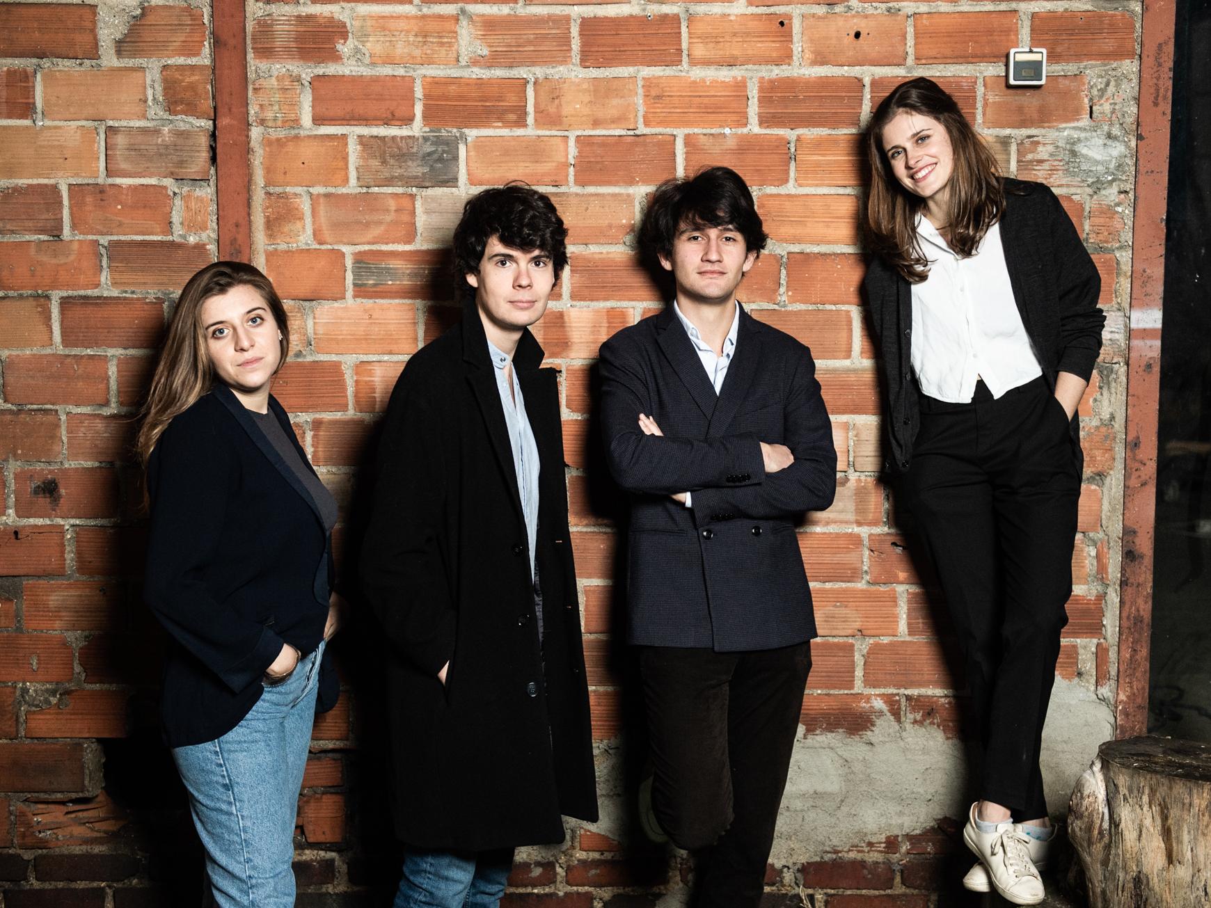 Four thirty-something white musicians stand against a brick wall.