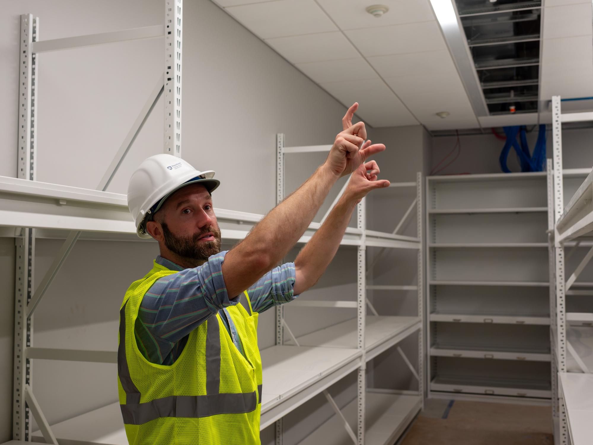 James Doyle wears a hardhat and construction vest while standing in a storage area. 