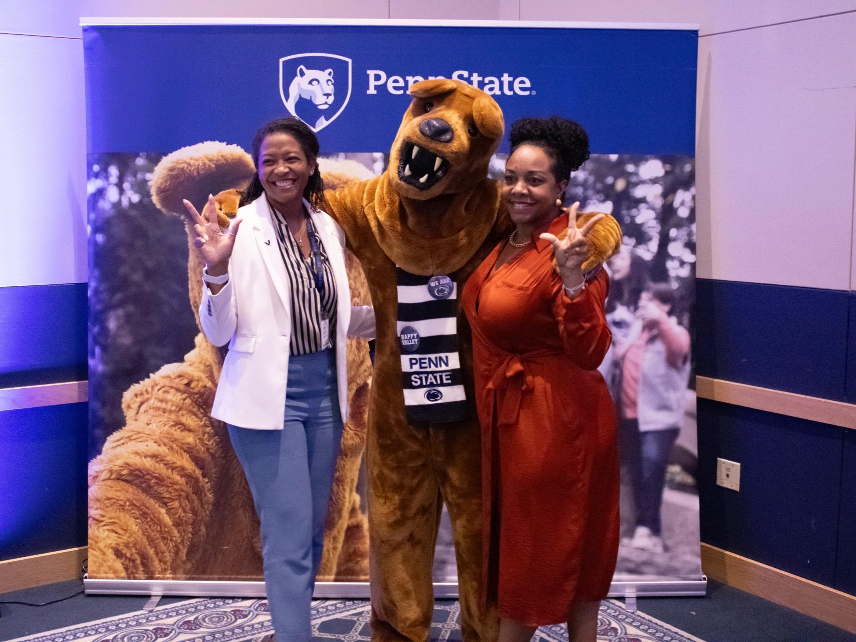 Two people in front of a Penn State backdrop with the Nittany Lion Mascot in the middle.