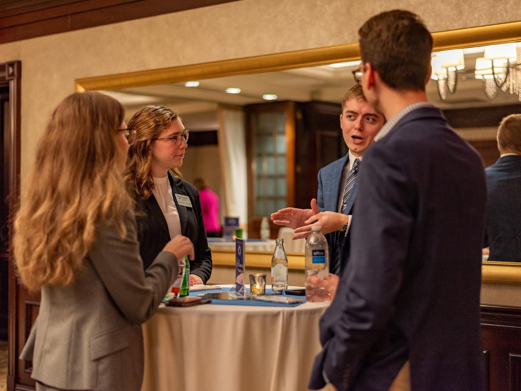 Four Liberal Arts students and alumni stand around a high-top table during a networking event at the City Club of Washington in September 2024.